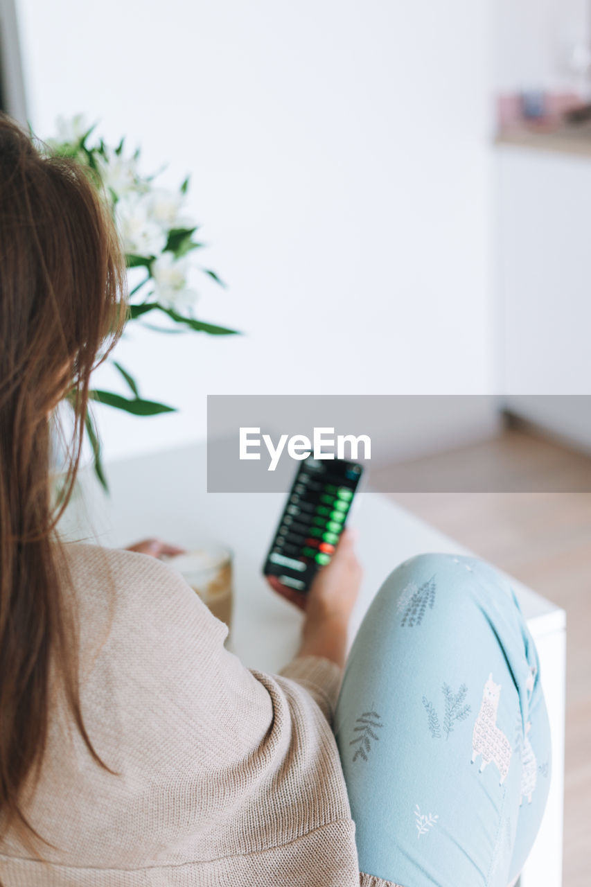 Young woman checking cryptocurrency charts and stock quotes on mobile phone with cup of coffee 