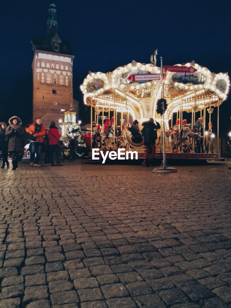 People on illuminated carousel on cobbled street