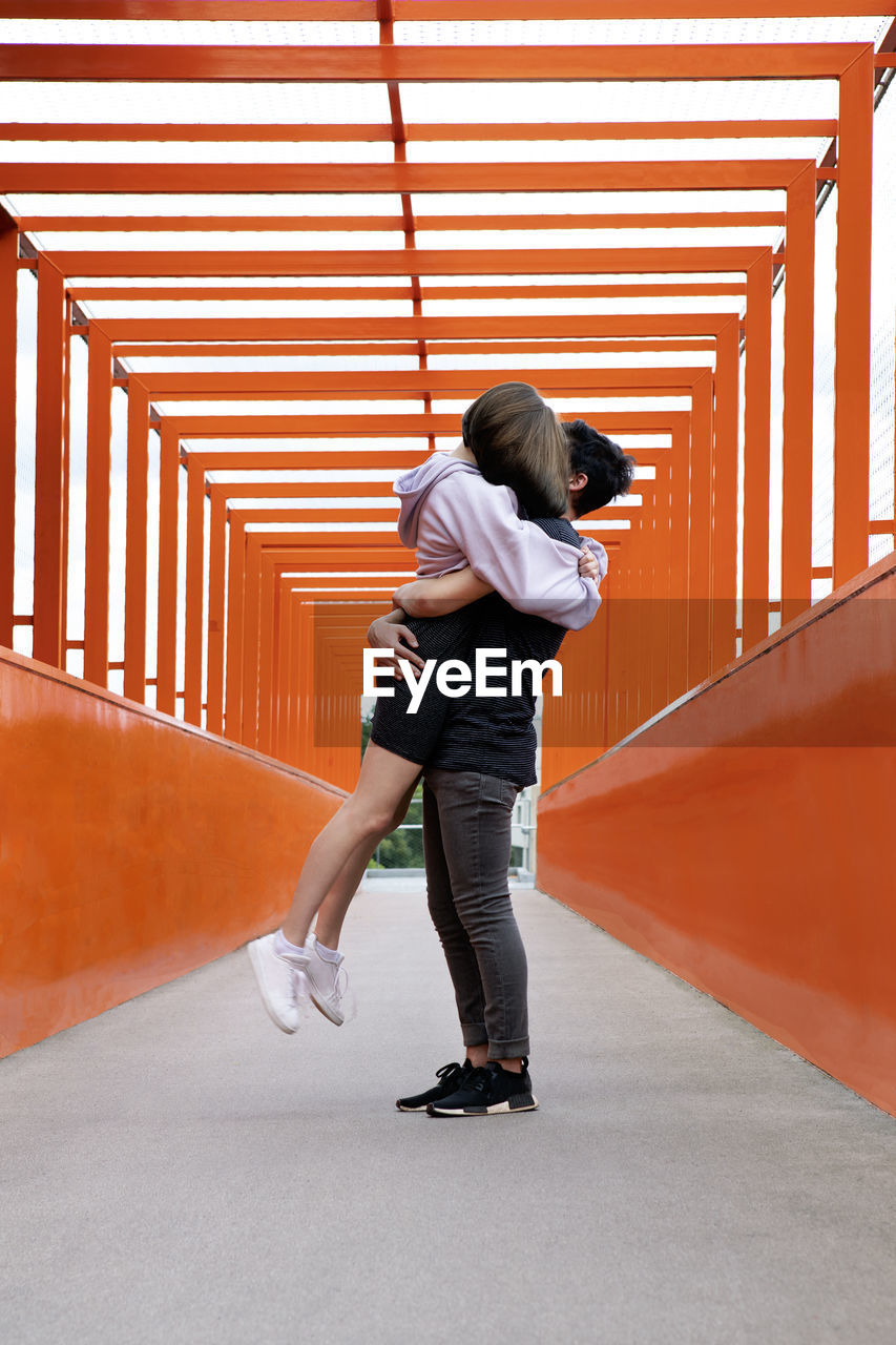Teenage boy picking up girlfriend on orange bridge