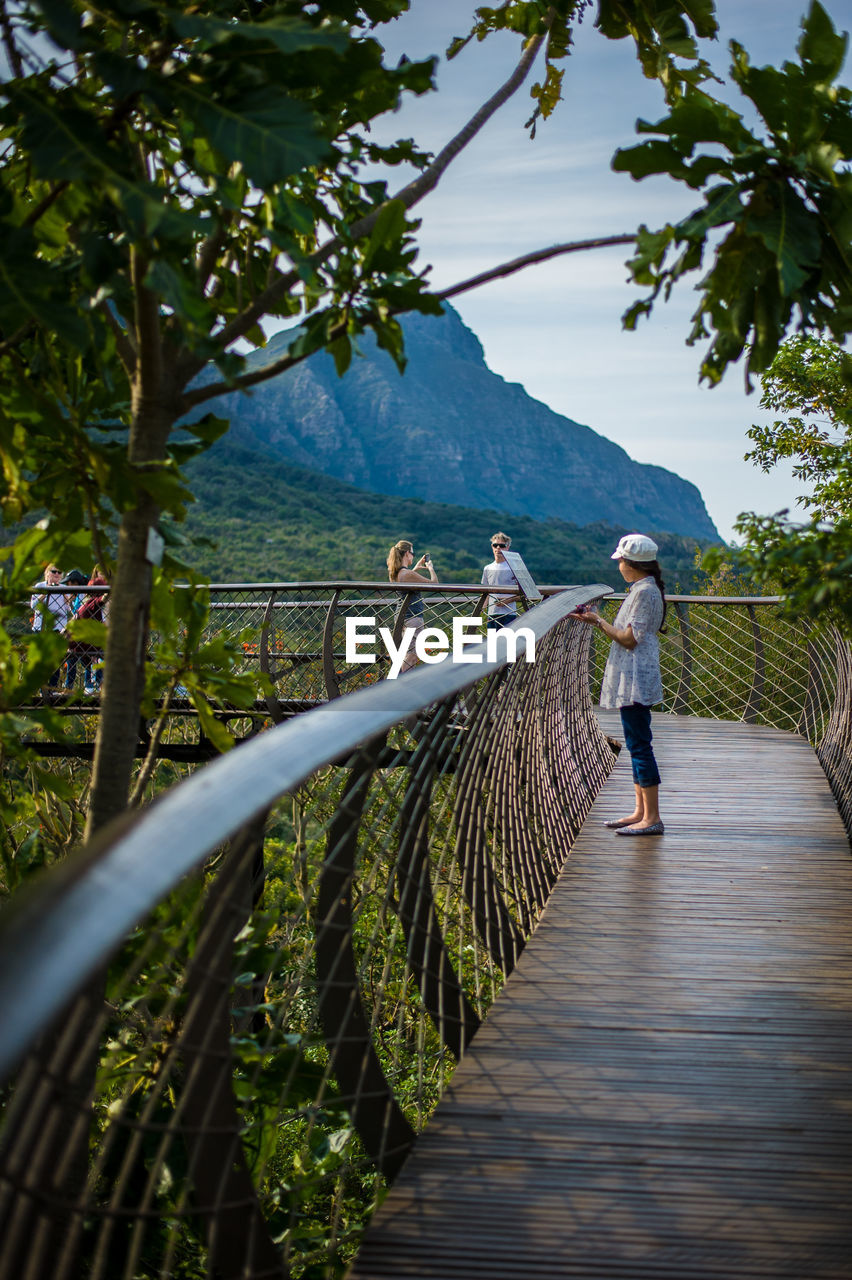 REAR VIEW OF TWO PEOPLE OVERLOOKING CALM LAKE AGAINST MOUNTAIN RANGE