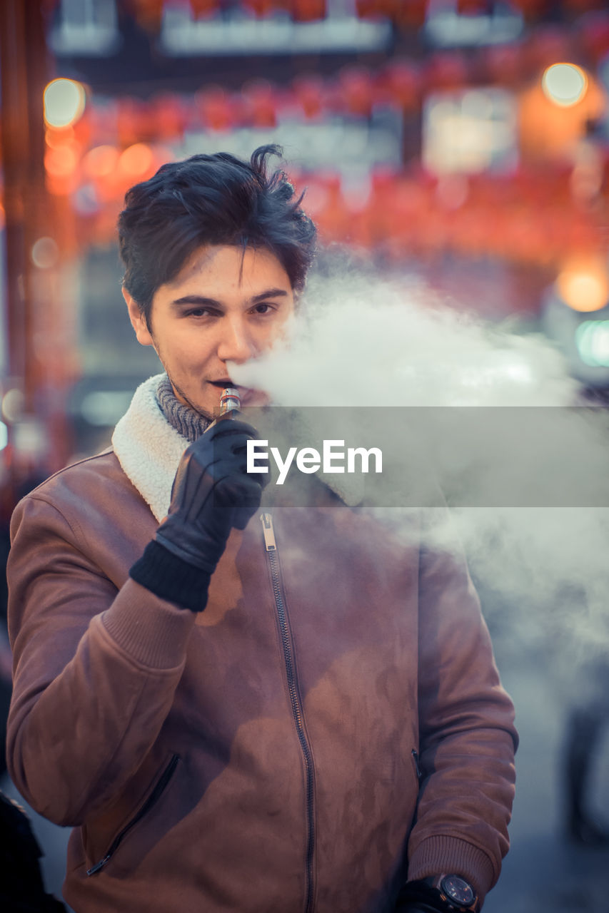 Portrait of young man smoking cigarette in city
