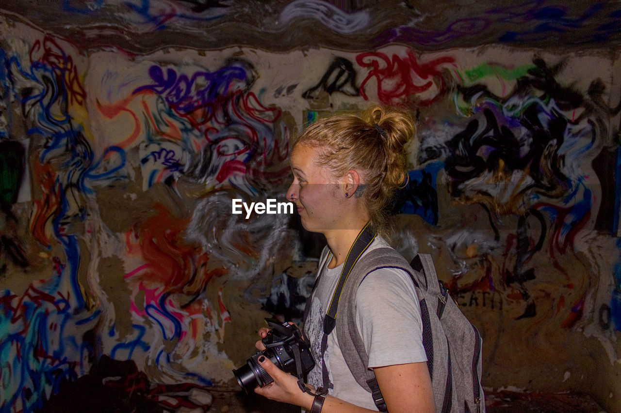 Woman holding camera against graffiti wall