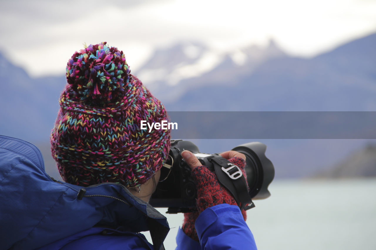 Side view of woman photographing with camera while standing against mountain