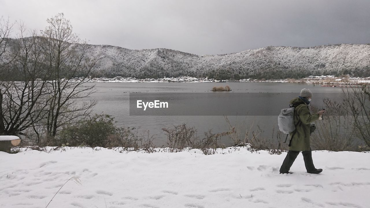 Side view of woman walking on snow covered field against sky