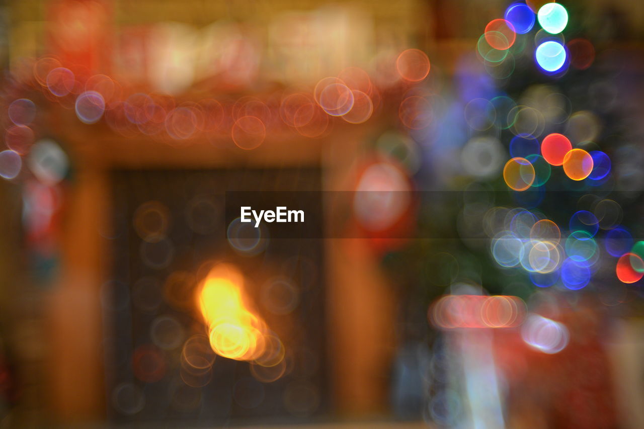 Defocused image of illuminated christmas tree by fireplace at home