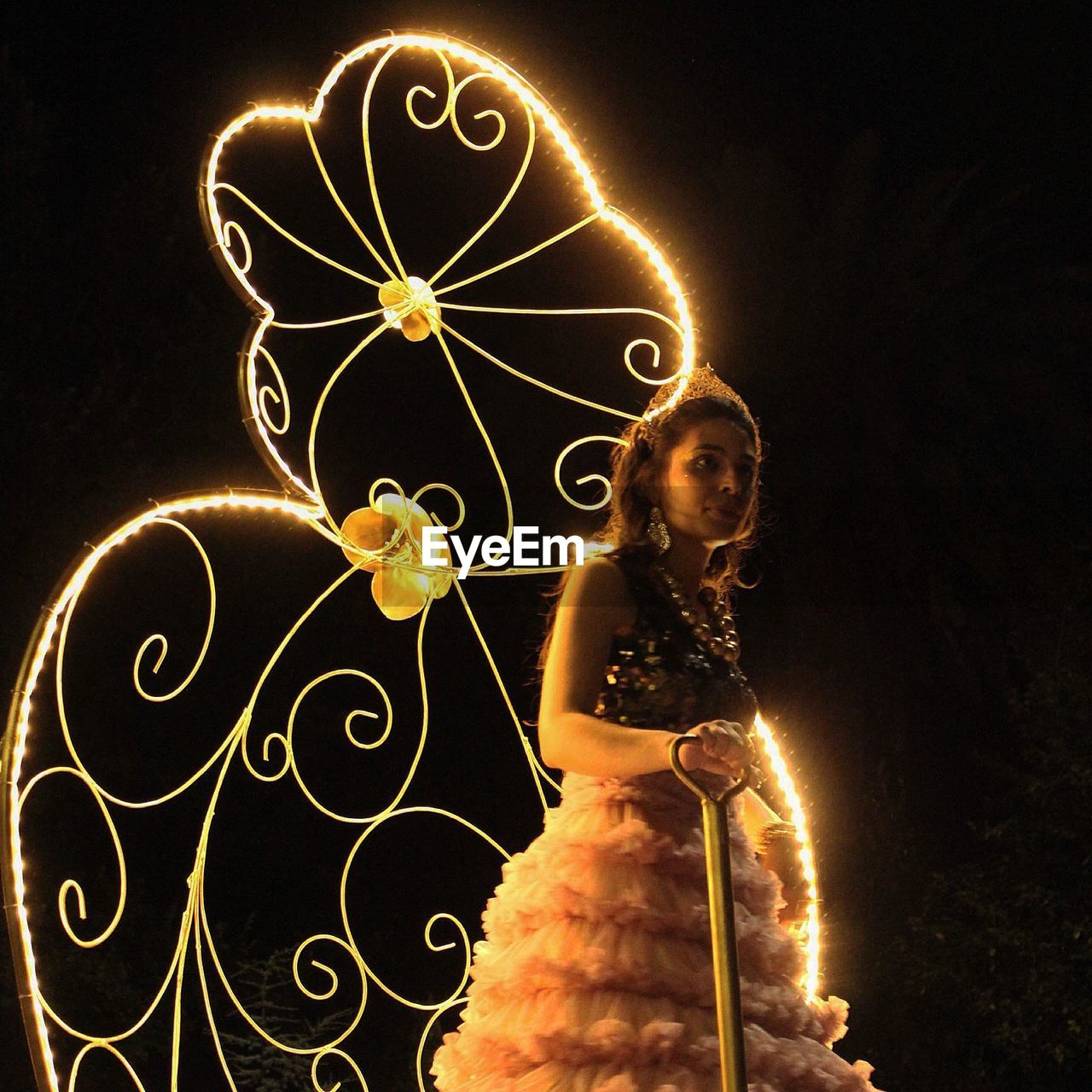 Mid adult woman wearing costume while standing against illuminated lights