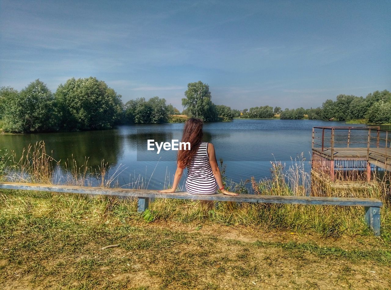 WOMAN BY LAKE AGAINST TREES