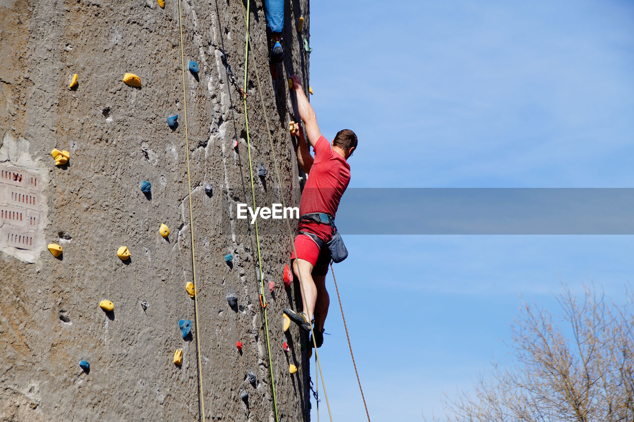 Low angle view of man rock climbing against sky