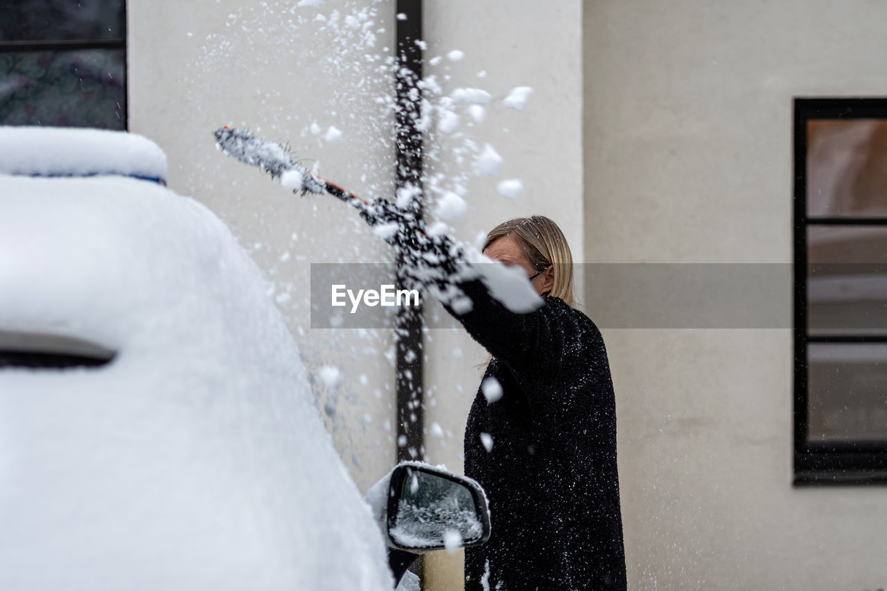 SIDE VIEW OF WOMAN STANDING AGAINST SNOW