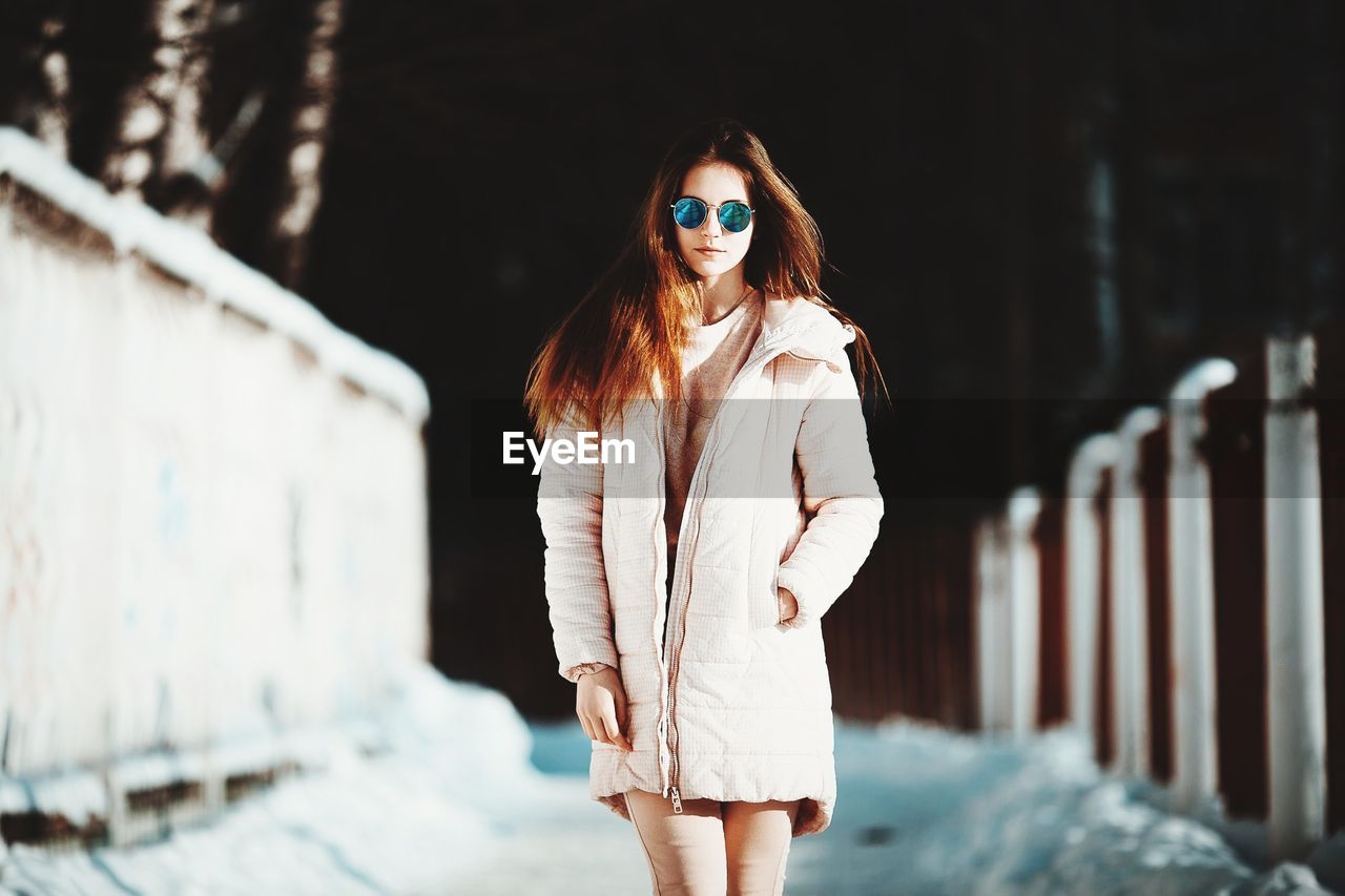 Portrait of young woman in warm clothing standing on footpath during winter