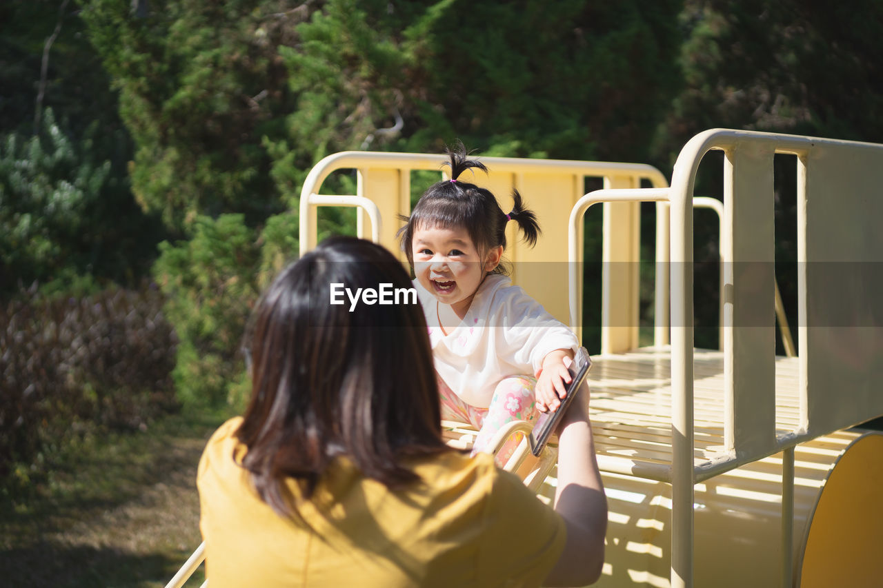 Rear view of mother playing with cheerful daughter at playground