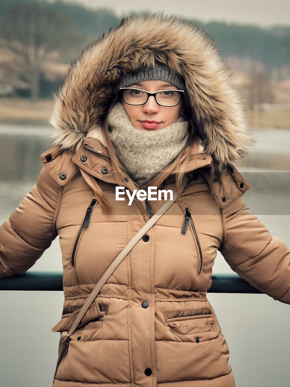 Portrait of woman standing against railing and lake during winter