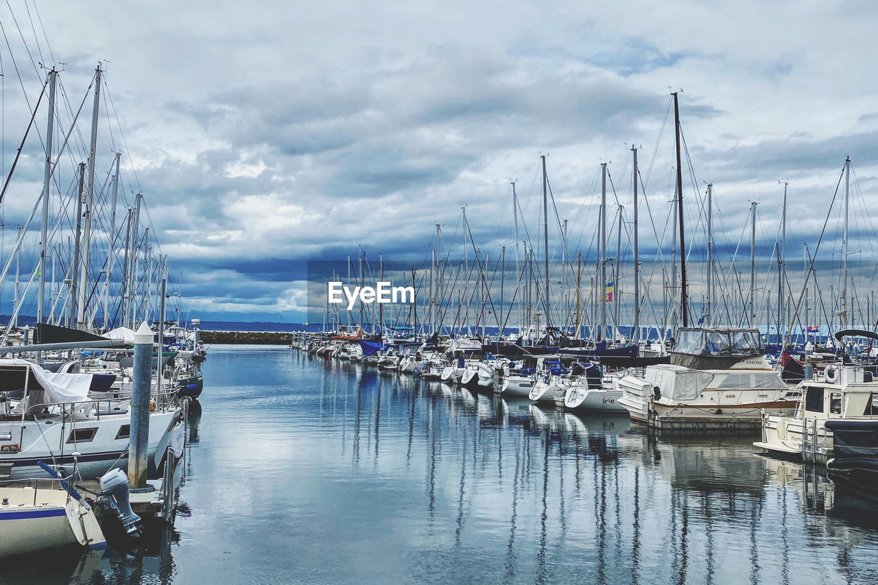 Sailboats moored at harbor in seattle against cloudy sky