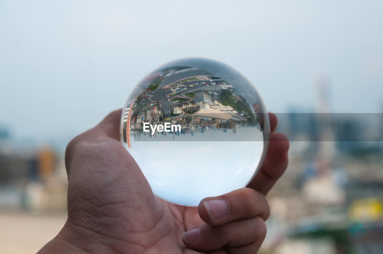 Close-up of hand holding crystal ball against sky