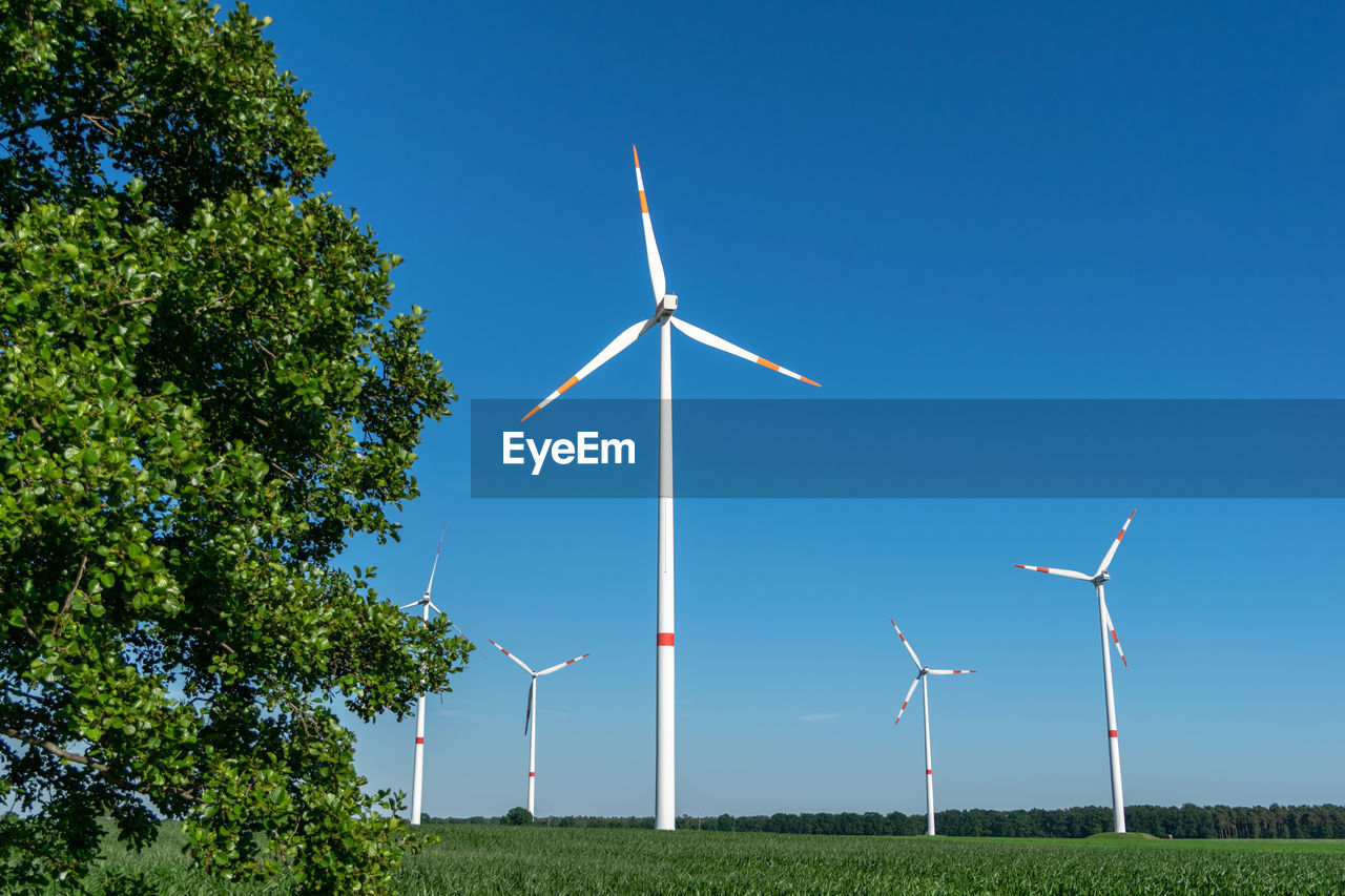 Five wind power turbines, part of a wind farm, on a green field near cottbus, brandenburg, germany.