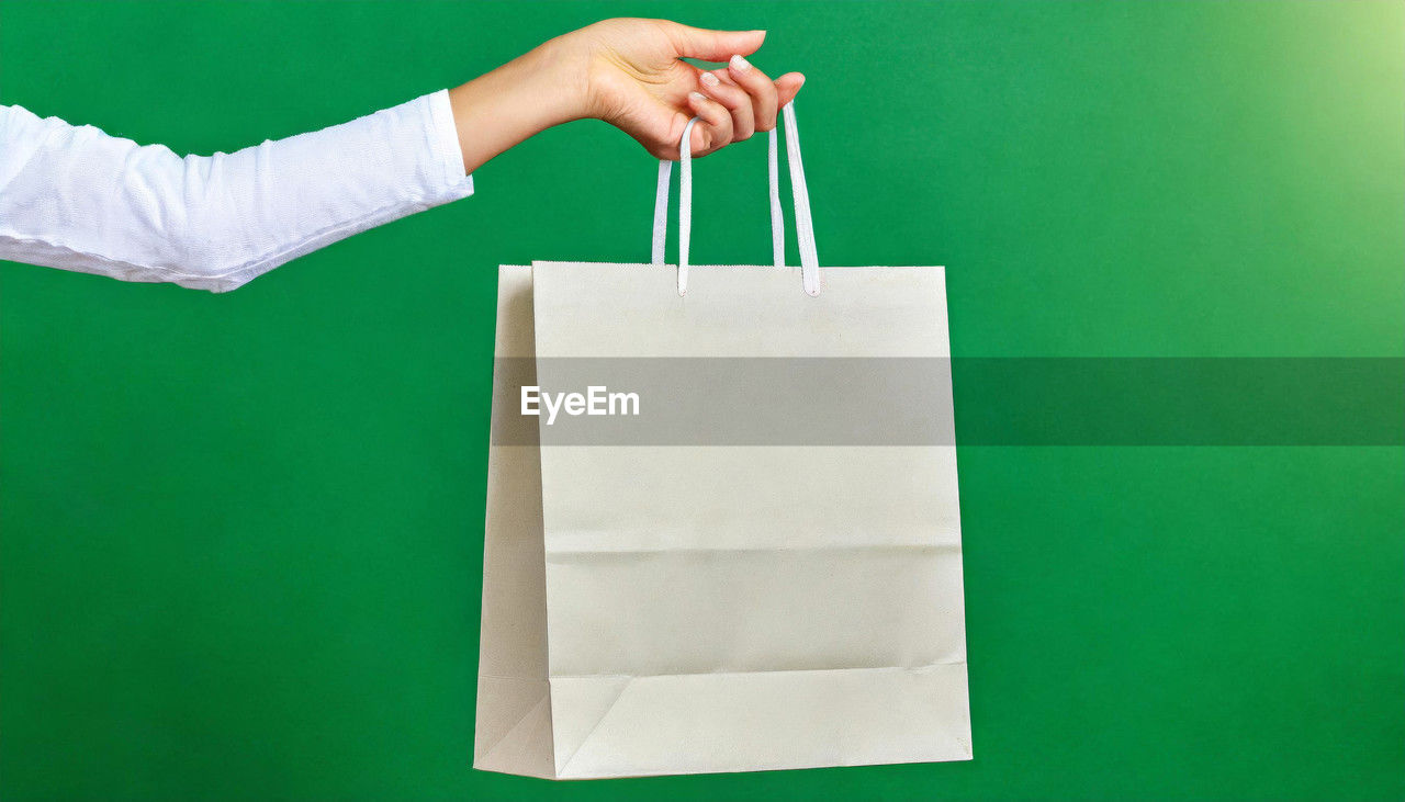 green background, green, shopping bag, handbag, tote bag, bag, hand, one person, colored background, copy space, holding, adult, business, retail, paper, shopping, indoors, studio shot, women, consumerism, paper bag