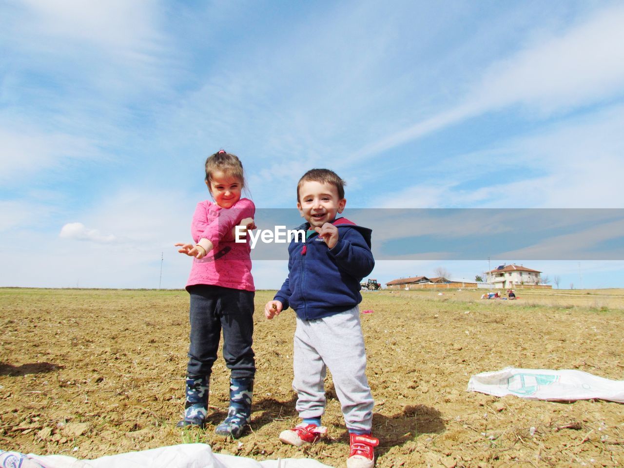 Portrait of happy siblings playing on field against sky