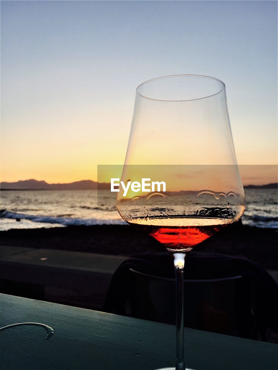 Close-up of wineglass on table at beach against sky during sunset
