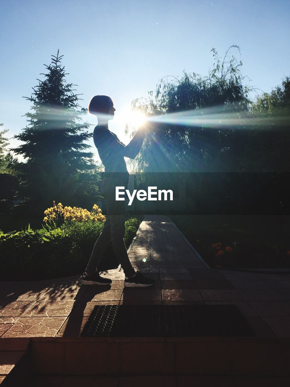 Optical illusion of young woman holding bright sun while standing on footpath at park