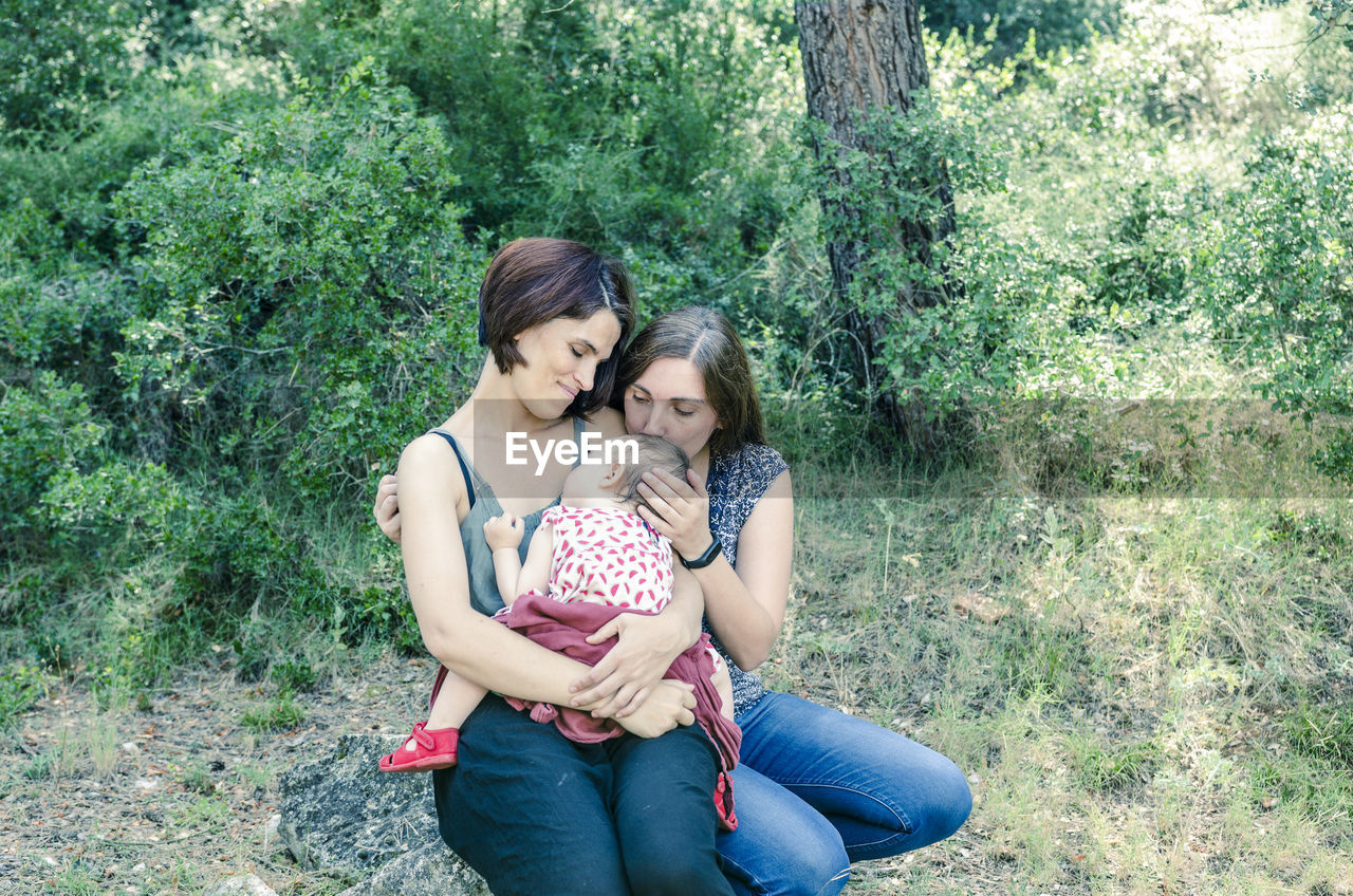 HAPPY YOUNG WOMAN WITH DAUGHTER SITTING ON GRASS