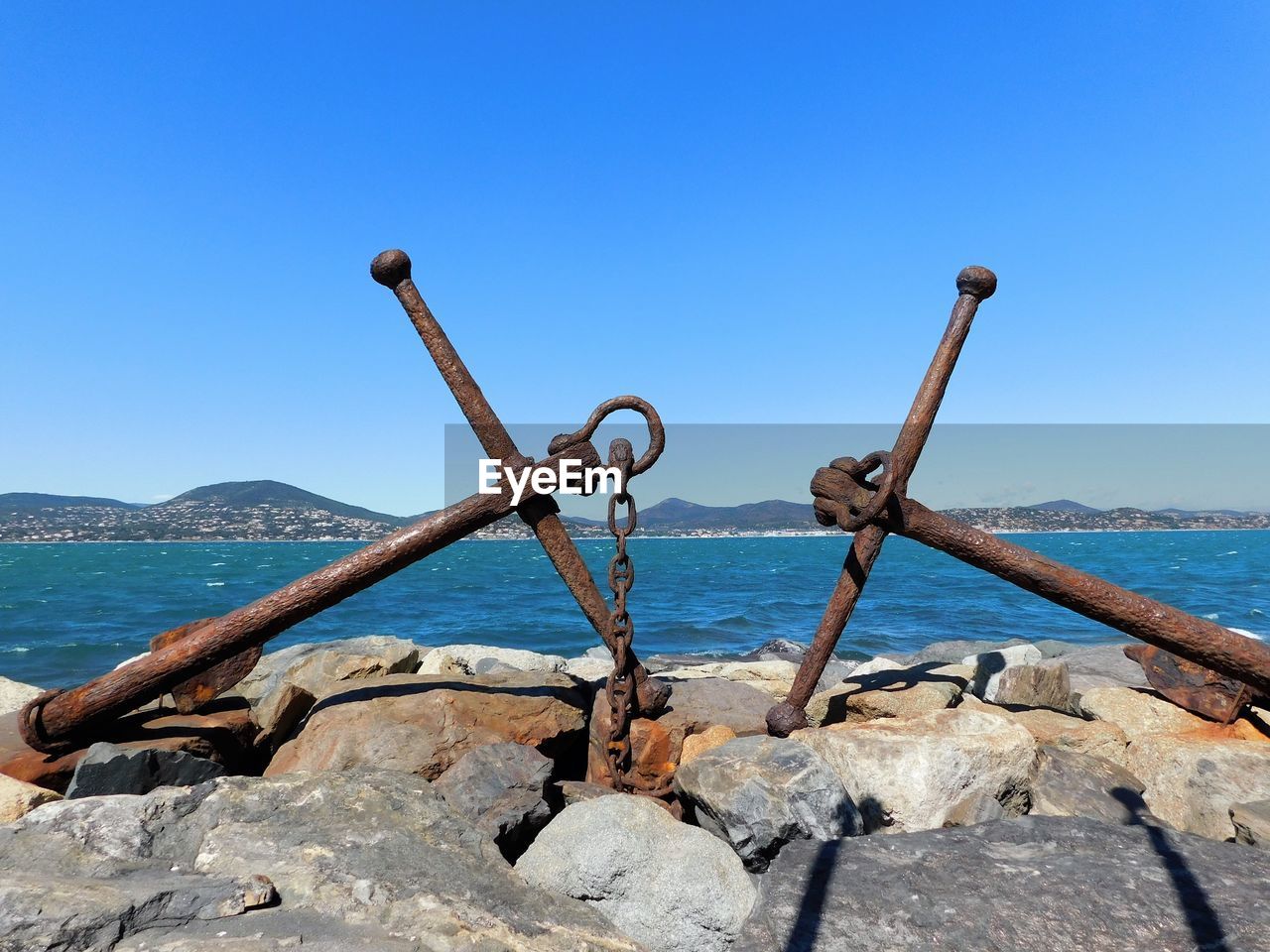 Double anchors on rocks by sea against clear blue sky