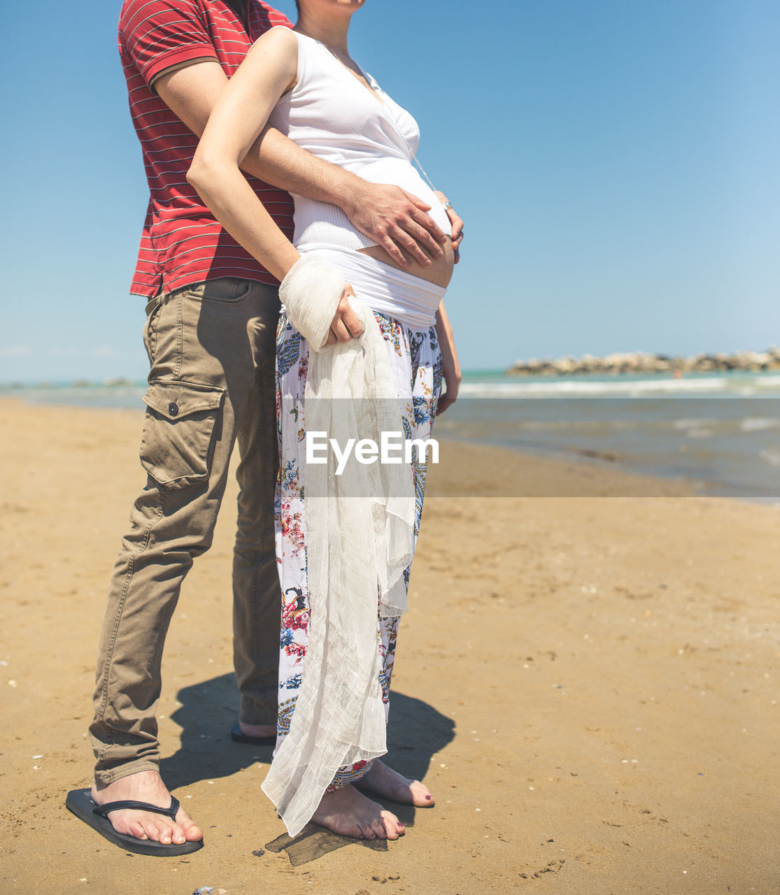 Low section of man holding pregnant woman belly at beach