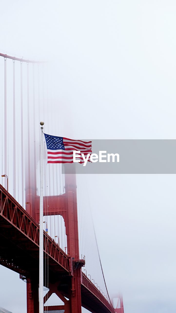 Low angle view of flag waving by bridge against sky during foggy weather