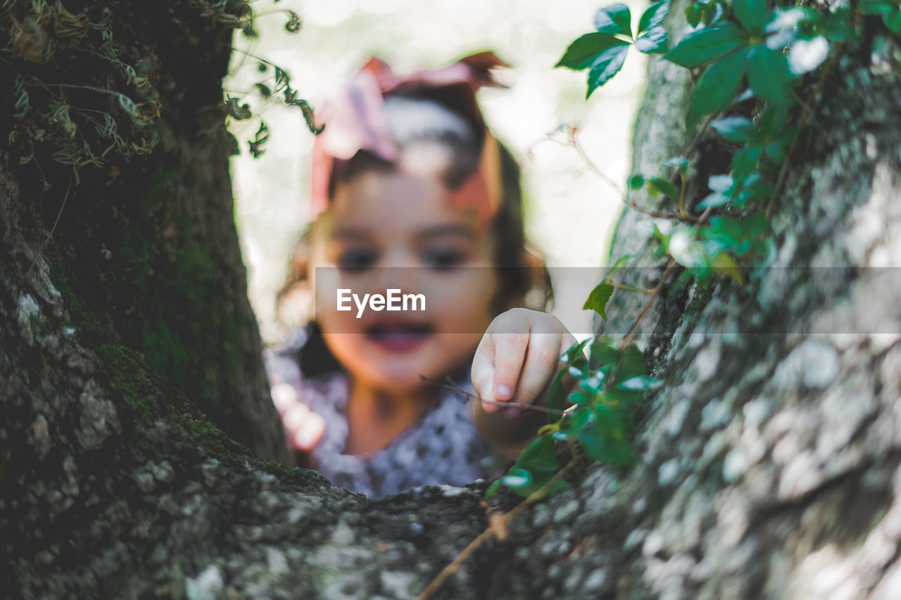 Cute girl picking stick standing by tree trunk