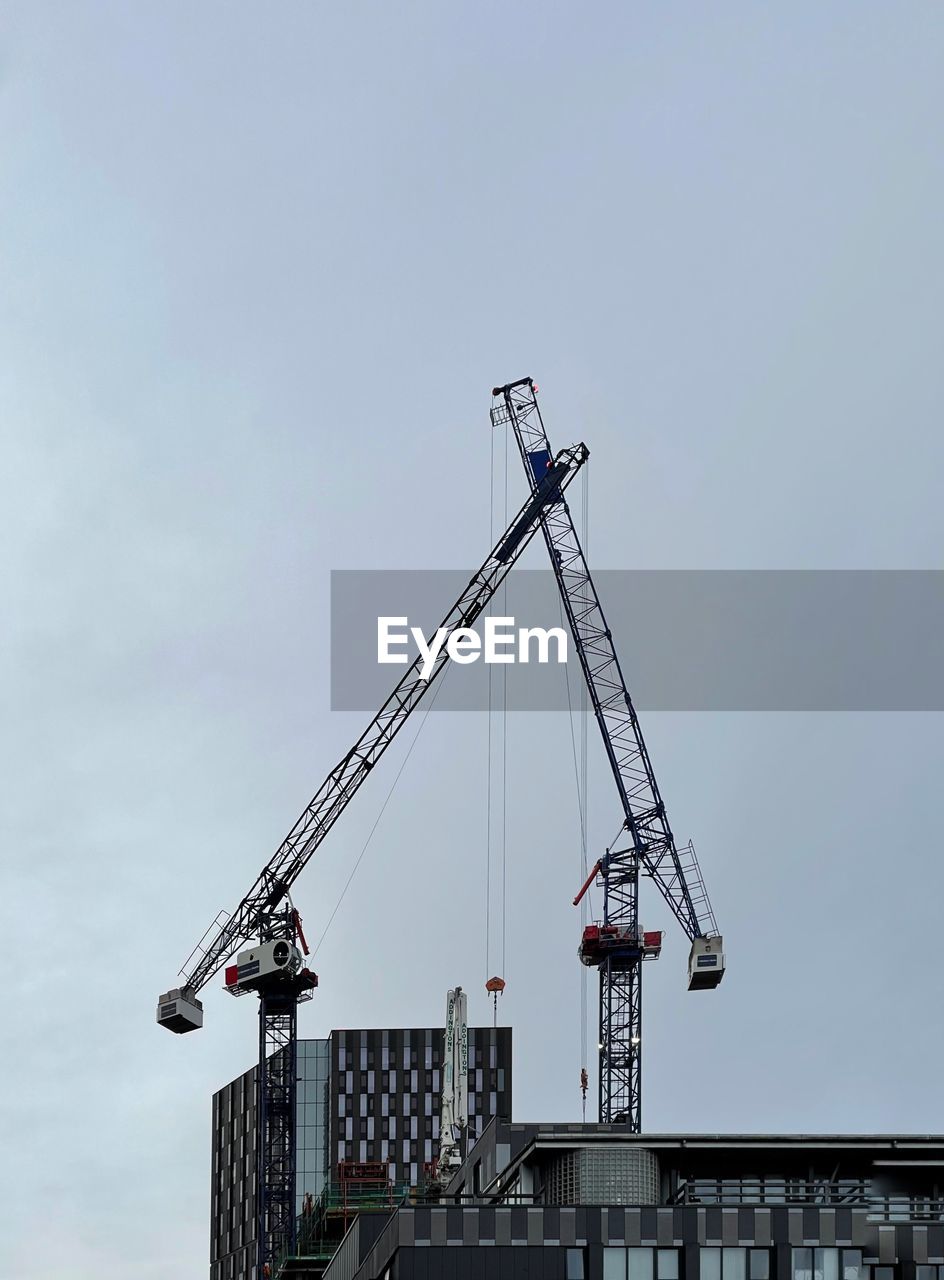 Low angle view of  two construction cranes  against sky