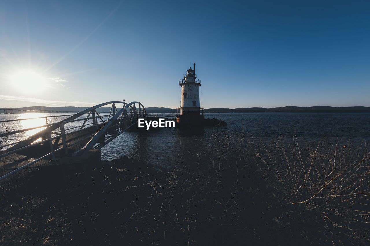 Bridge over sea by lighthouse against clear sky