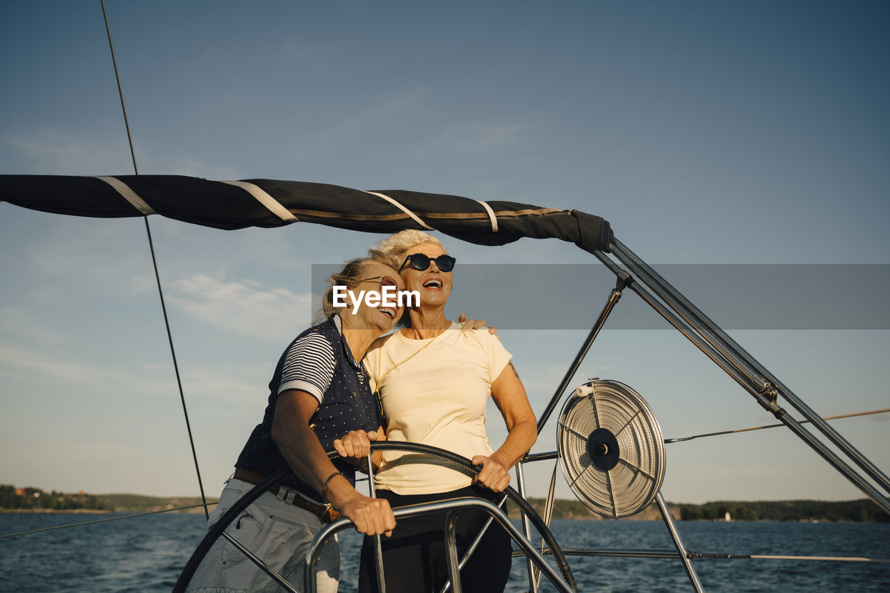 Cheerful female friends looking away while standing in boat against sky