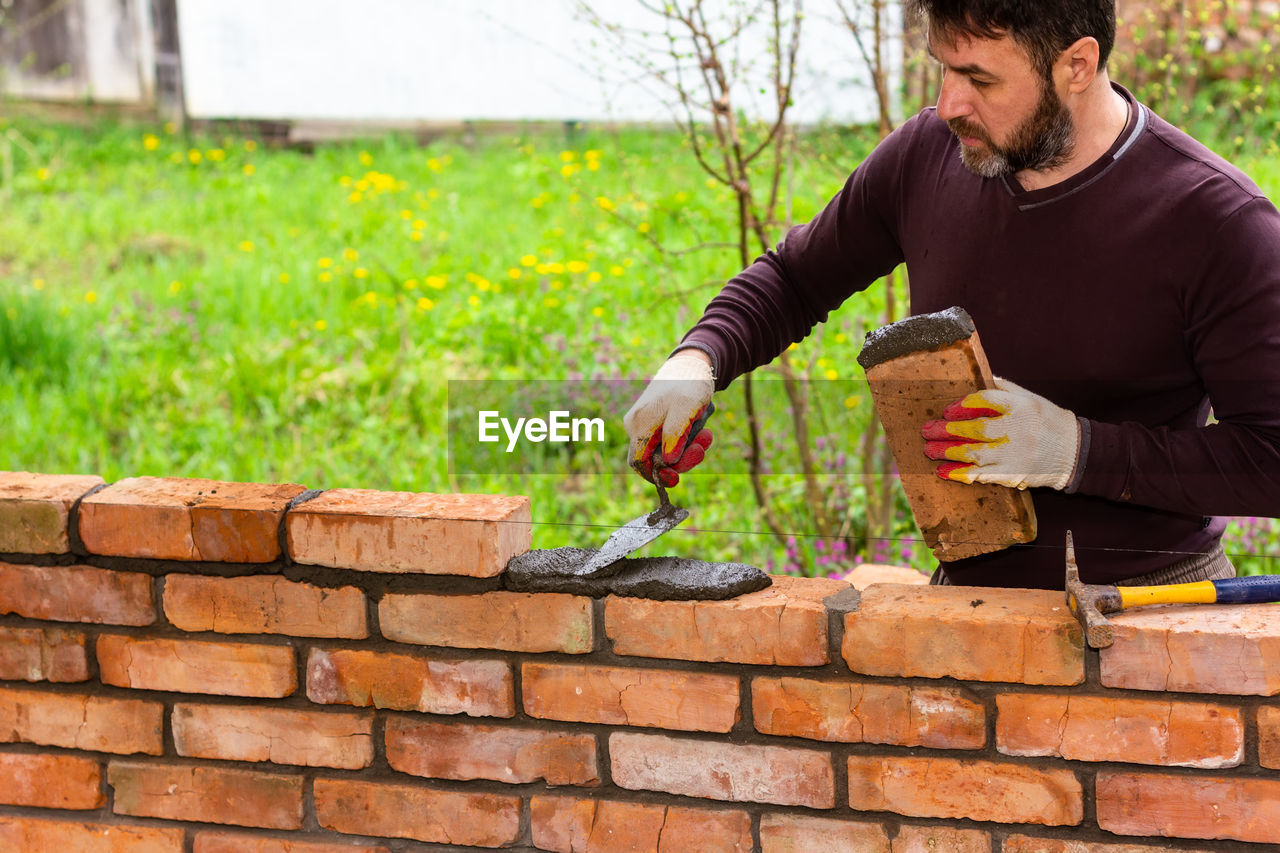 A man builds a wall of bricks, lays a brick on a cement-sand mortar