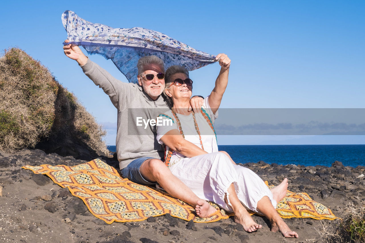 Couple in sunglasses with scarf sitting at beach