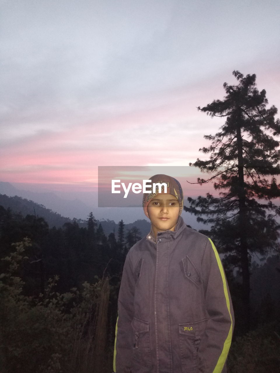 Portrait of boy standing in forest during sunset