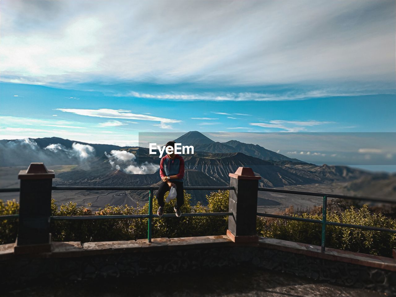 Man standing by railing on mountain against sky