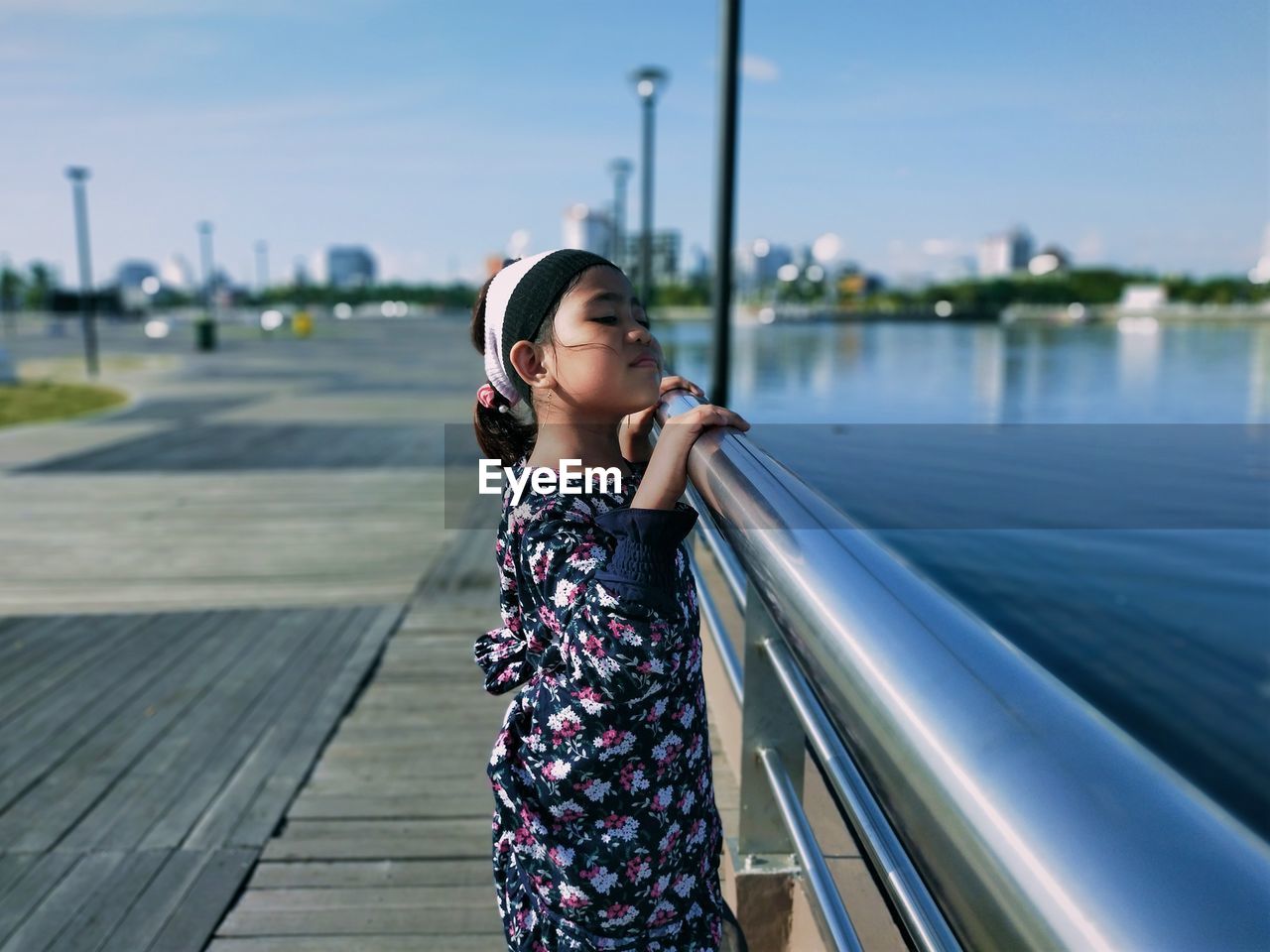 Full length of young woman standing on railing against sky