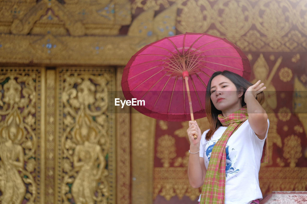 Woman holding pink umbrella while standing against historic building