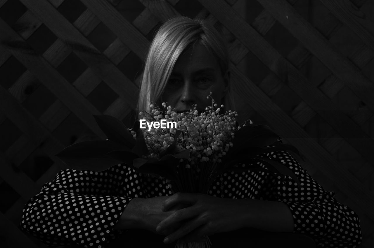 Close-up of woman holding flowers against black background