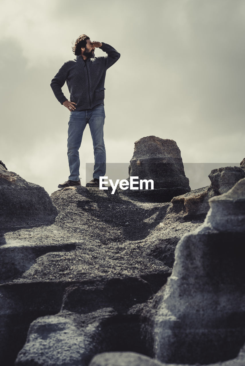 rear view of man standing on rock against sky