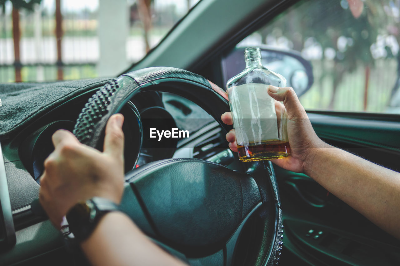 Hand of man driving car by holding alcohol bottle