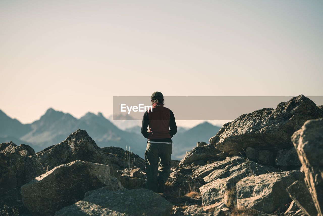 Rear view of man standing on rock against clear sky