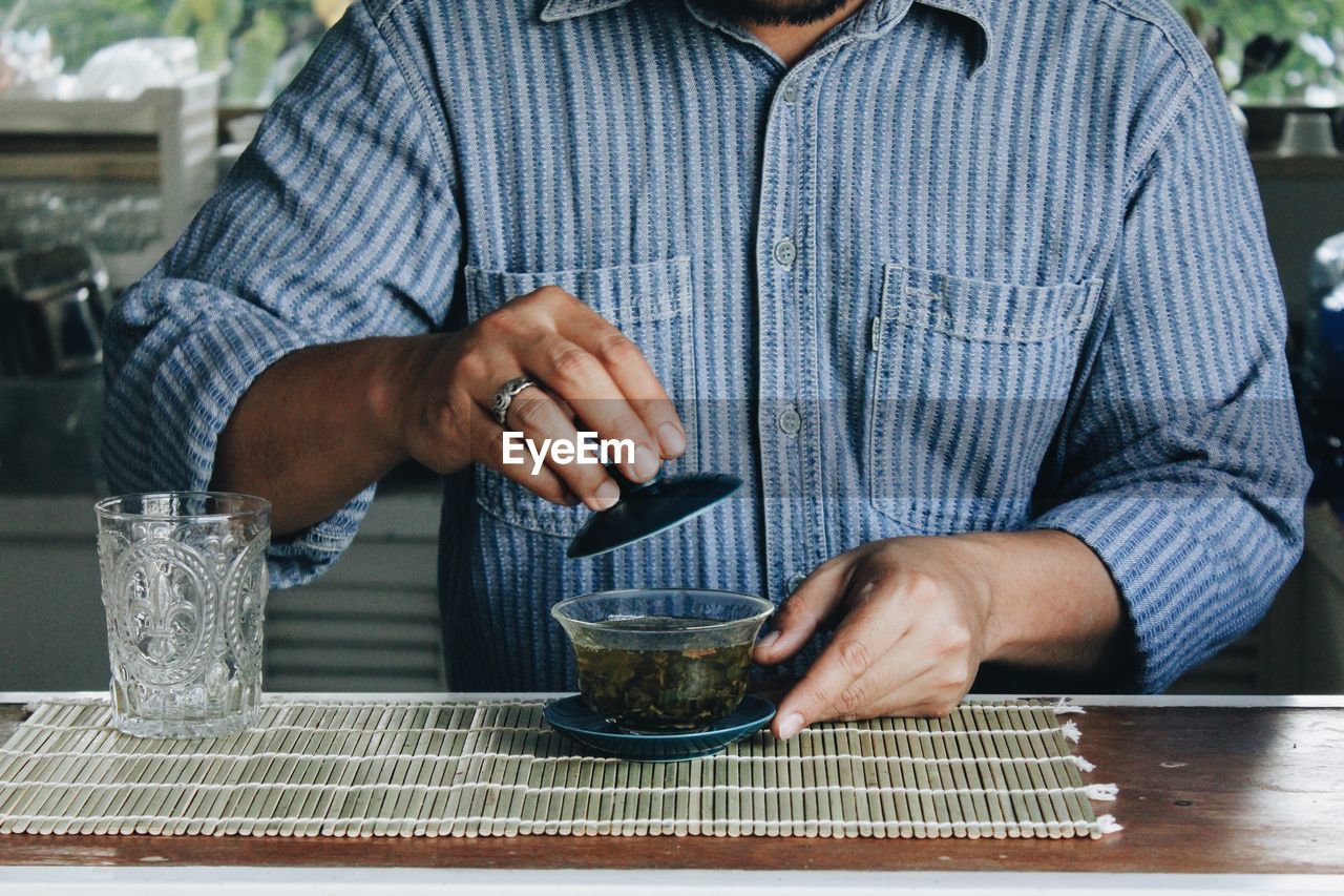 MIDSECTION OF MAN HOLDING COFFEE CUP WITH TABLE