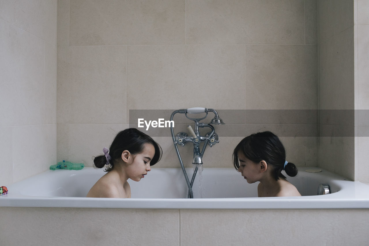 Twin sister bathing together in bathtub at home