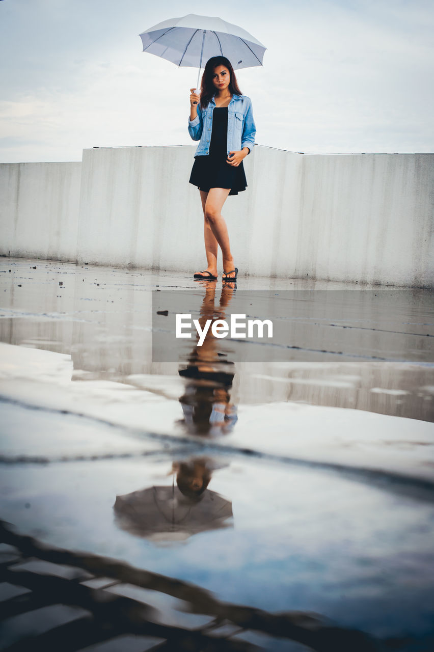 Full length of young woman standing on building terrace during rainy season