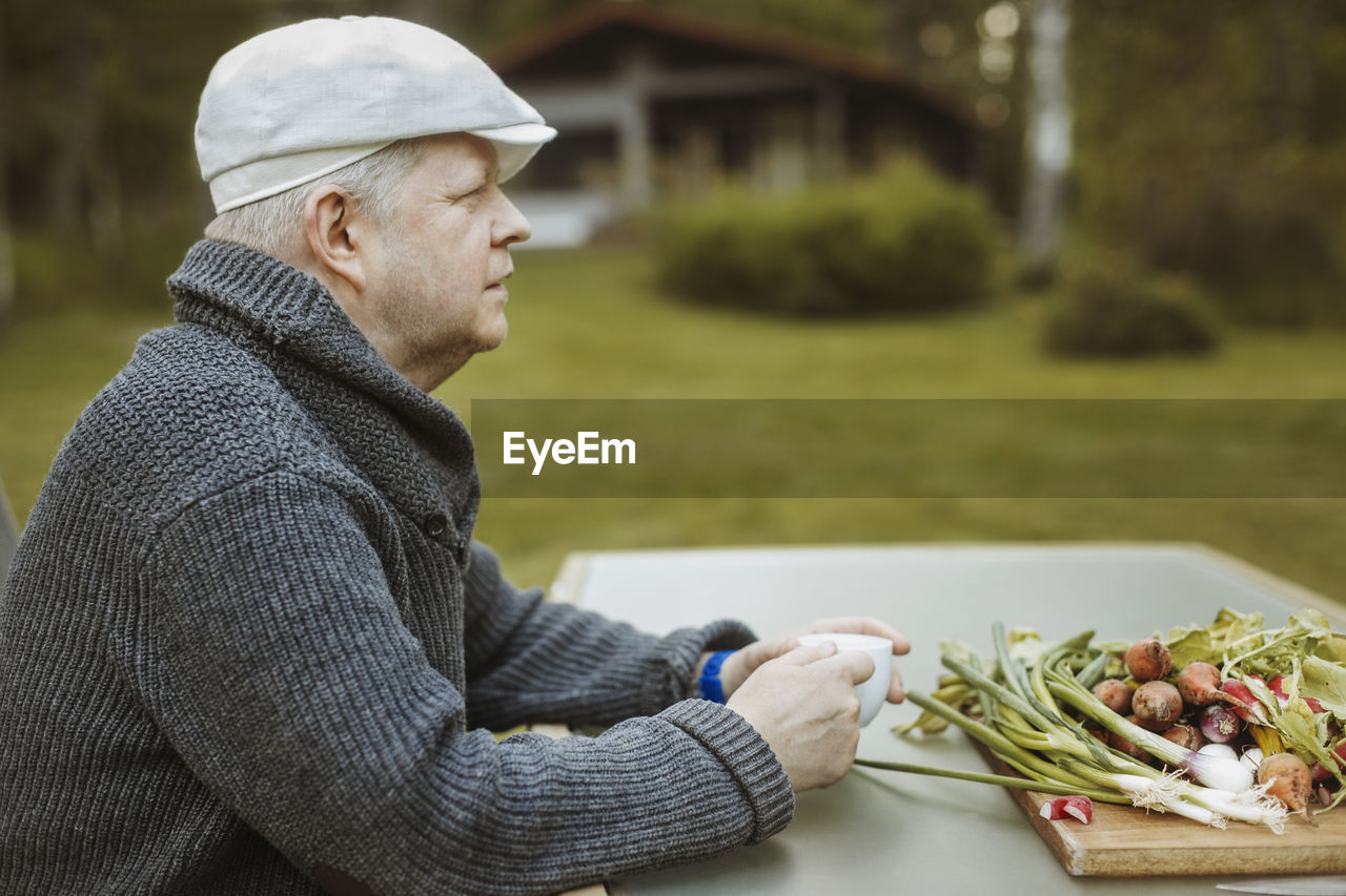 Side view of mature man sitting at table with freshly harvested vegetables