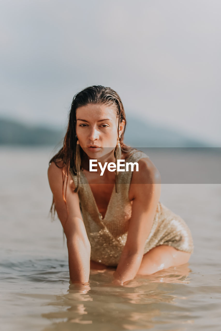 water, one person, adult, women, sea, young adult, land, clothing, nature, portrait, trip, vacation, holiday, relaxation, beach, photo shoot, hairstyle, female, brown hair, swimwear, summer, leisure activity, long hair, bikini, swimming, sky, front view, lifestyles, wet, outdoors, looking at camera, human leg, day, looking, sand, emotion, person, skin, wet hair, wellbeing, limb, smiling, tranquility, enjoyment, copy space, travel, waist up, sitting, serious, fashion, beauty in nature, happiness, environment, portrait photography, three quarter length, contemplation, human face