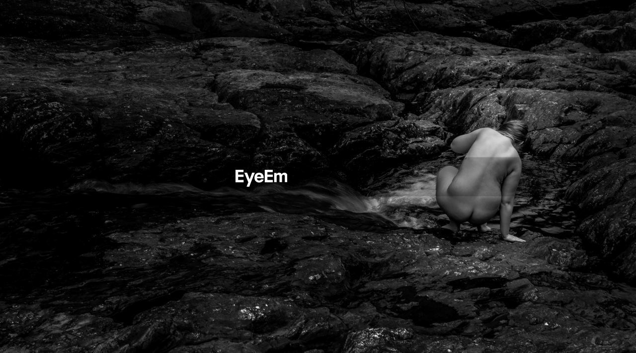 Rear view of naked woman crouching on rock
