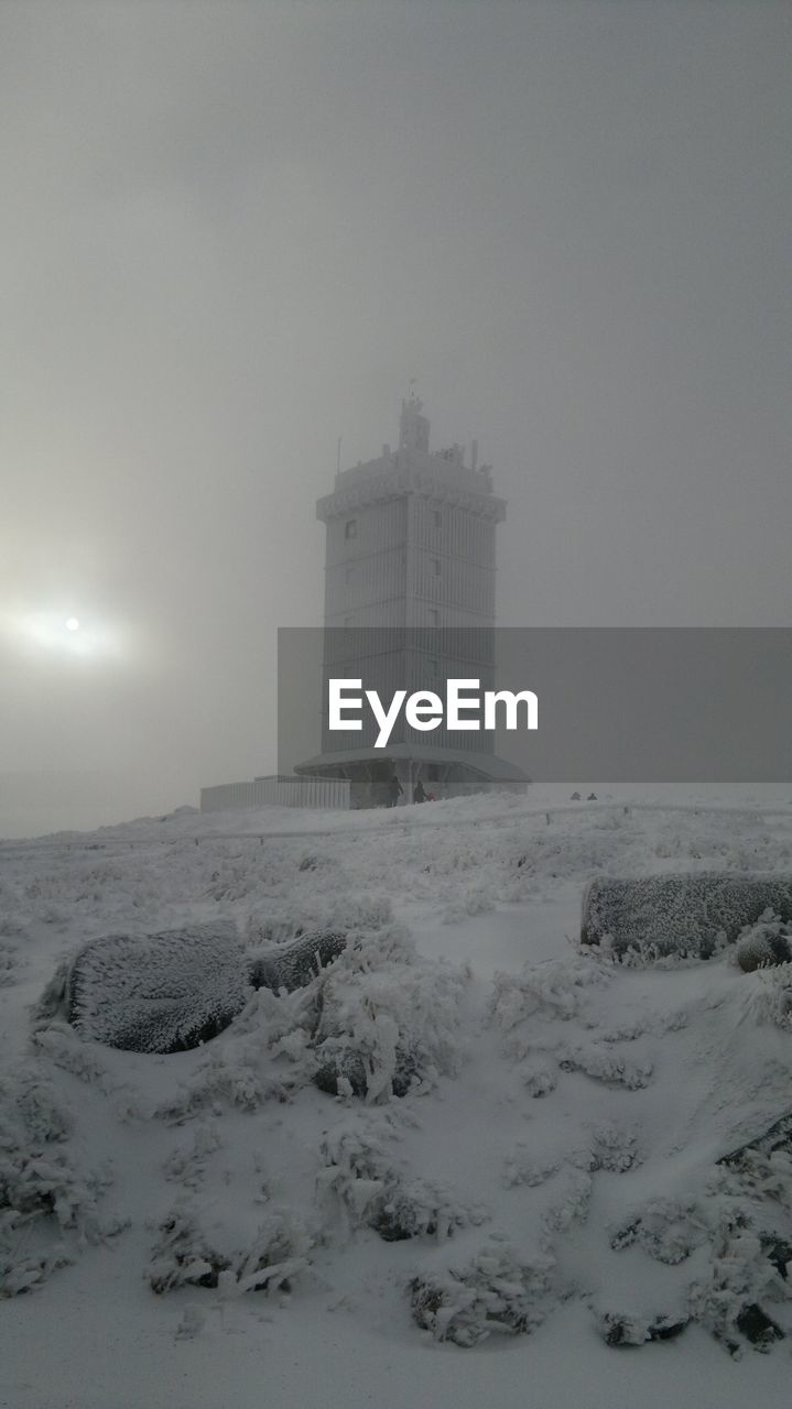 Snow covered land by buildings against sky during winter