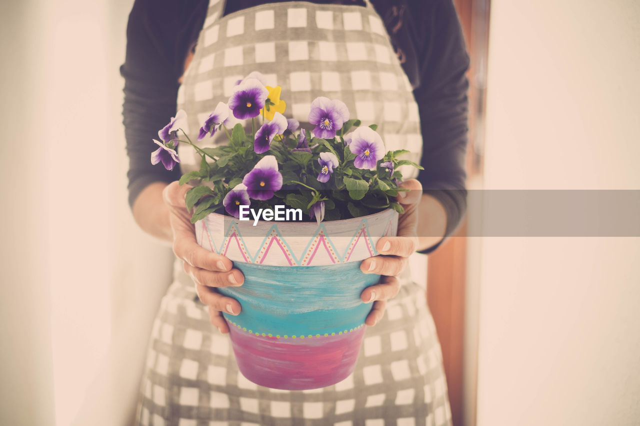Midsection of woman holding potted plant while standing against wall