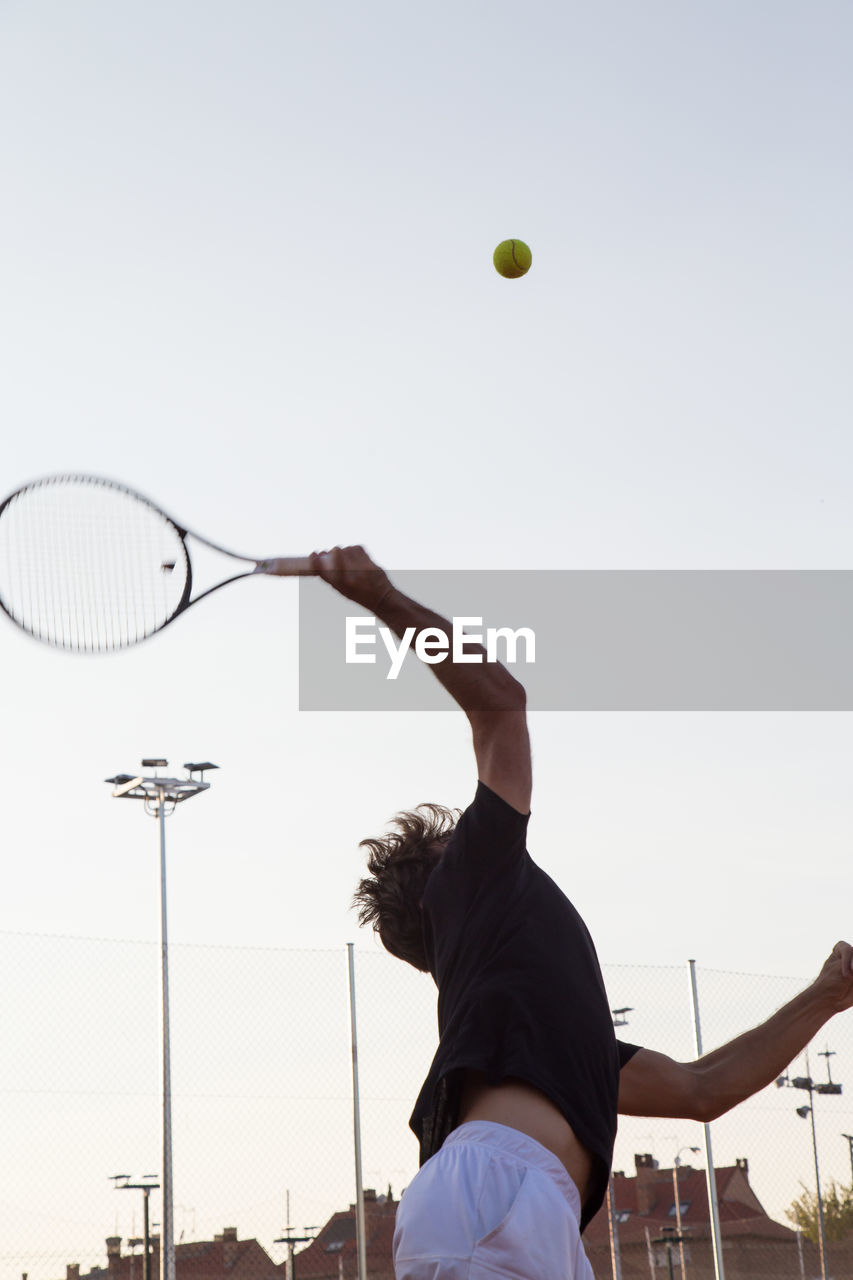 Man playing tennis on court against clear sky